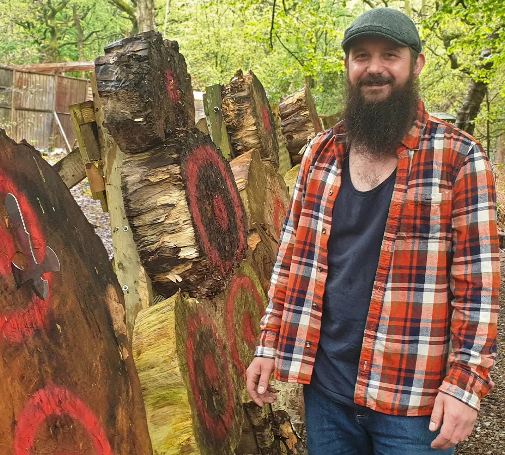 Happy man posing with a throwing knife in a large wooden target on Adventure Now's throwing range