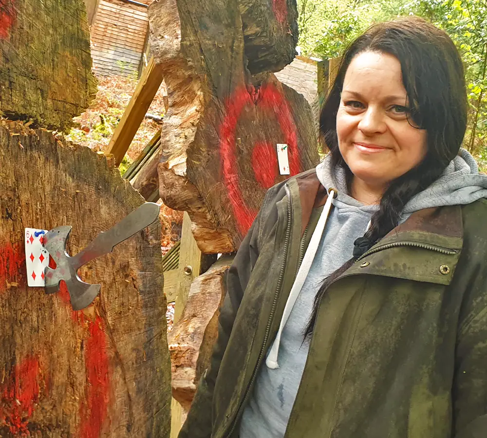 Lady with a throwing knife stuck in a card on a large wooden outdoor target