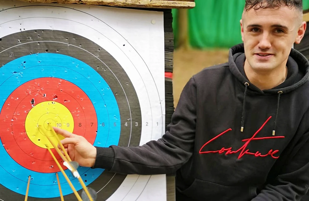 Smiling man pointing to several arrows stuck in the bullseye of an archery target