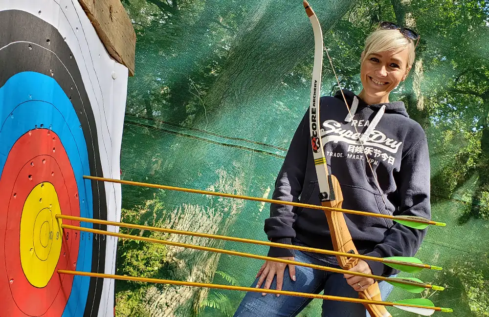 Smiling lady posing with Archery target with arrows in the bullseye at Adventure Now Manchester