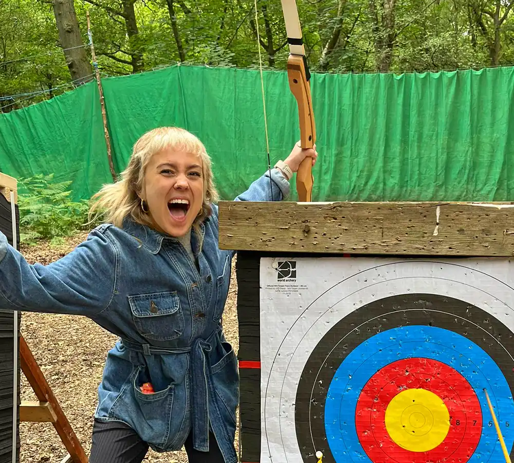 Girl screaming with excitement holding a bow, next to an archery target