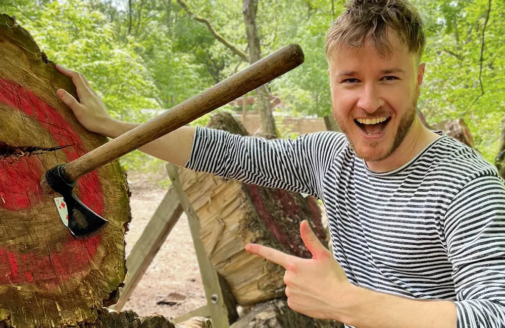 Smiling man pointing at a throwing axe stuck in a wooden target at Adventure Now Manchester