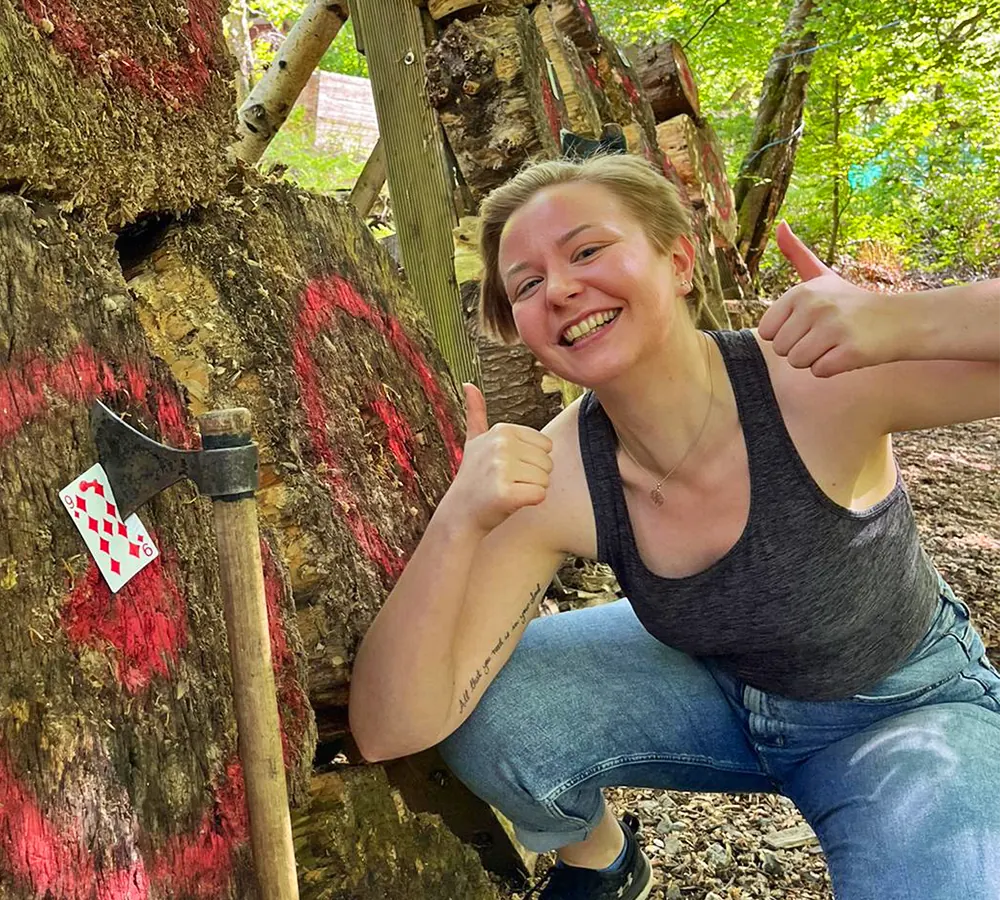 Excited lady giving a 'thumbs up' whilst outdoor axe throwing