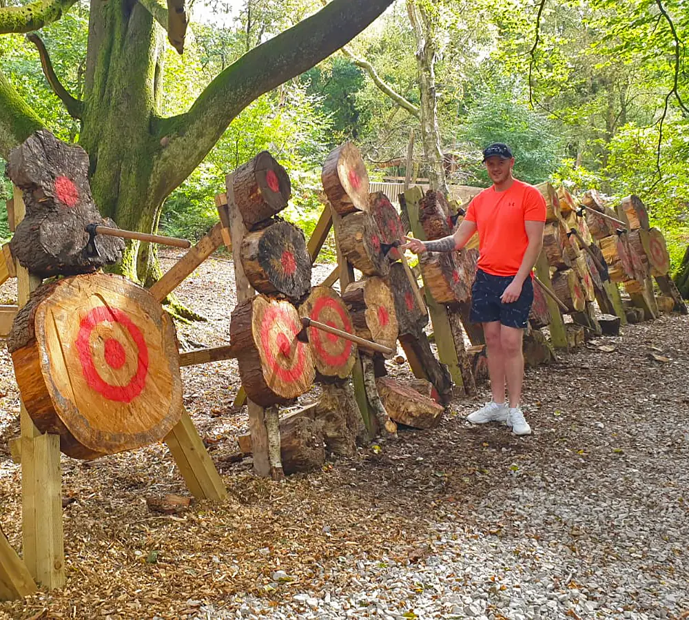 Smiling man pointing at throwing axes stuck in wooden axe targets