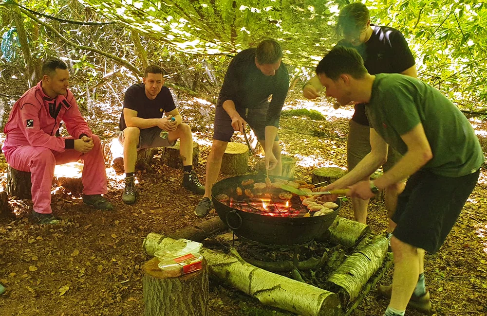 Group of friends around an outdoor BBQ in a woodland cooking sausages and burgers