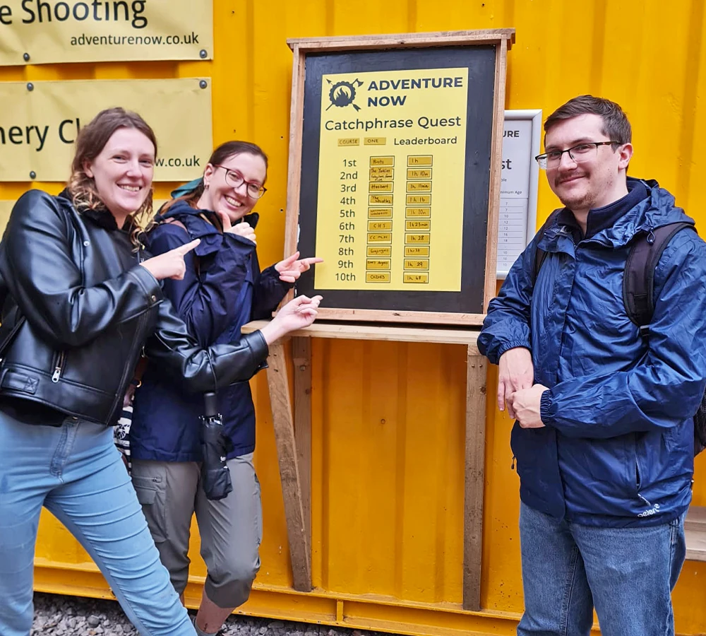 Three friends smiling and pointing at the catchphrase quest leaderboard