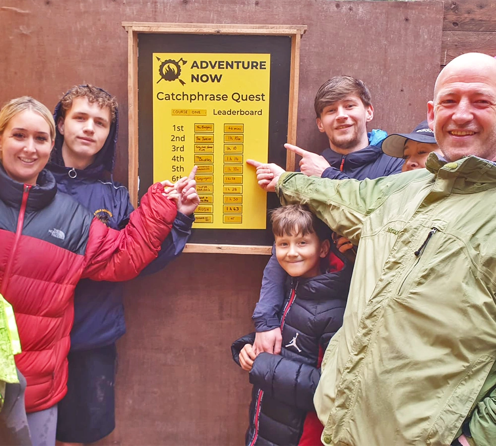 A family group pointing at their team's place on the orienteering activity leaderboard