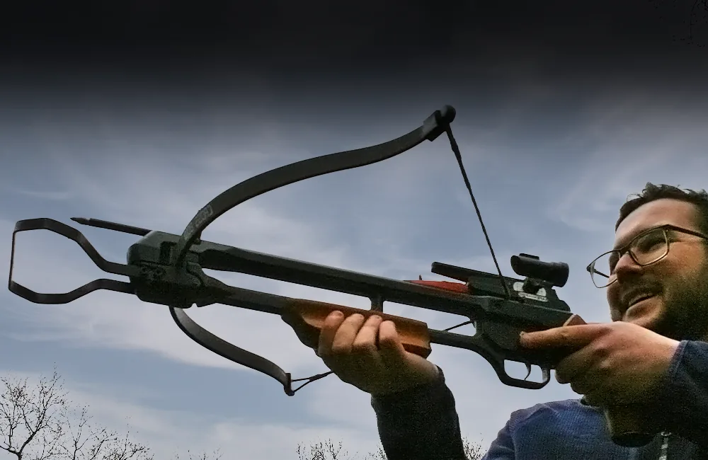 Crossbow being aimed by a smiling man, with trees in the background