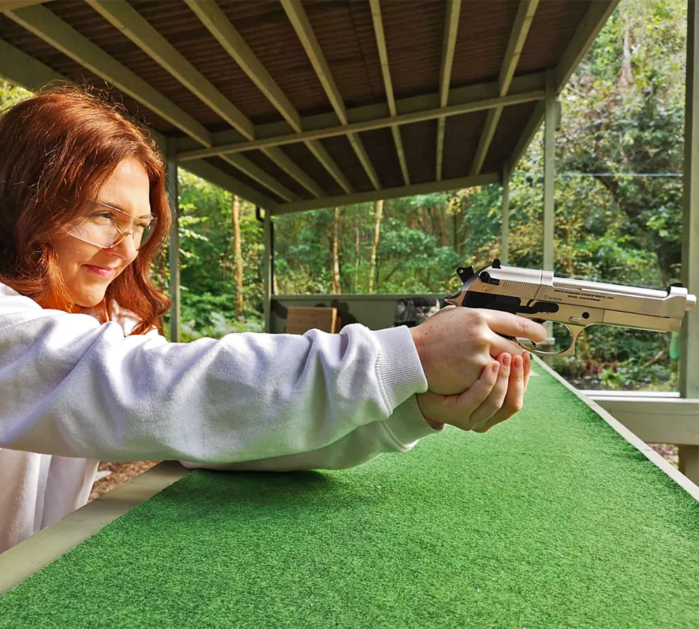 Smiling lady shooting a silver Beretta air pistol in the woodland at Adventure Now