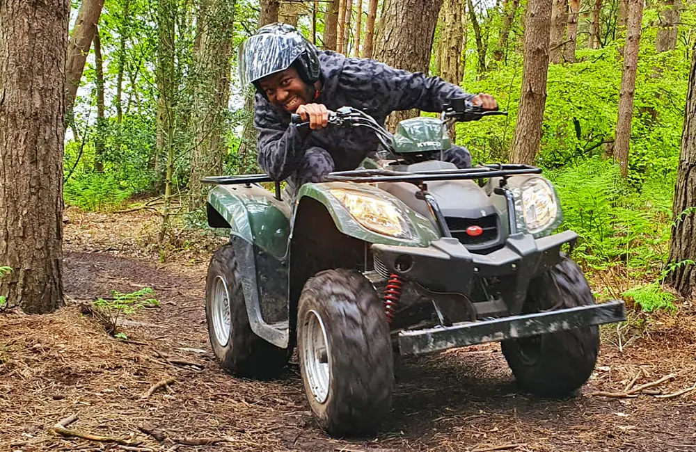 Action shot of smiling man riding a quad bike on a woodland track in Manchester