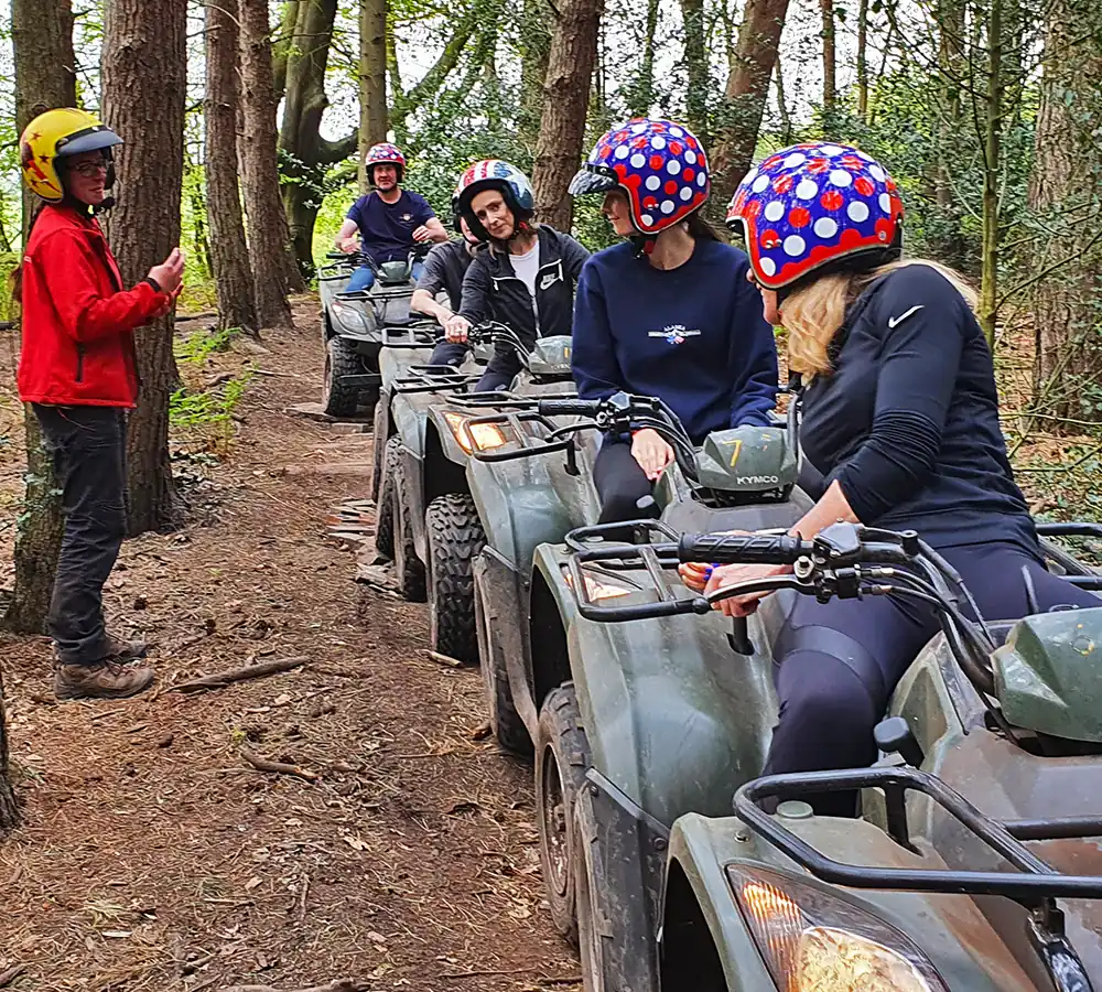 Quad biking group receiving briefing from an instructor whilst sat on their ATVs in an open woodland