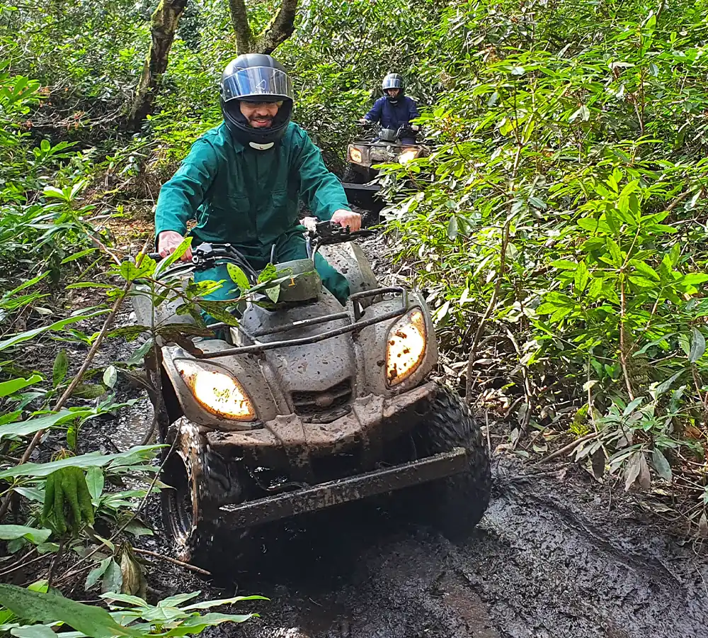 Two excited people riding on an off-road quad bike trail in a bushy woodland