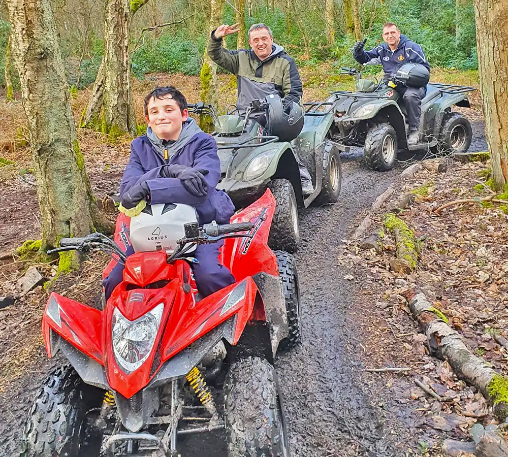 Child sat on a smaller quad bike, two adults in the background sat of full size quad bikes