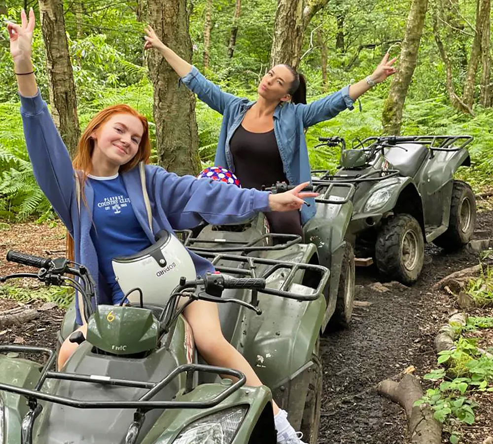 Two smiling girls sat posing on ATVs after completing a course in Manchester