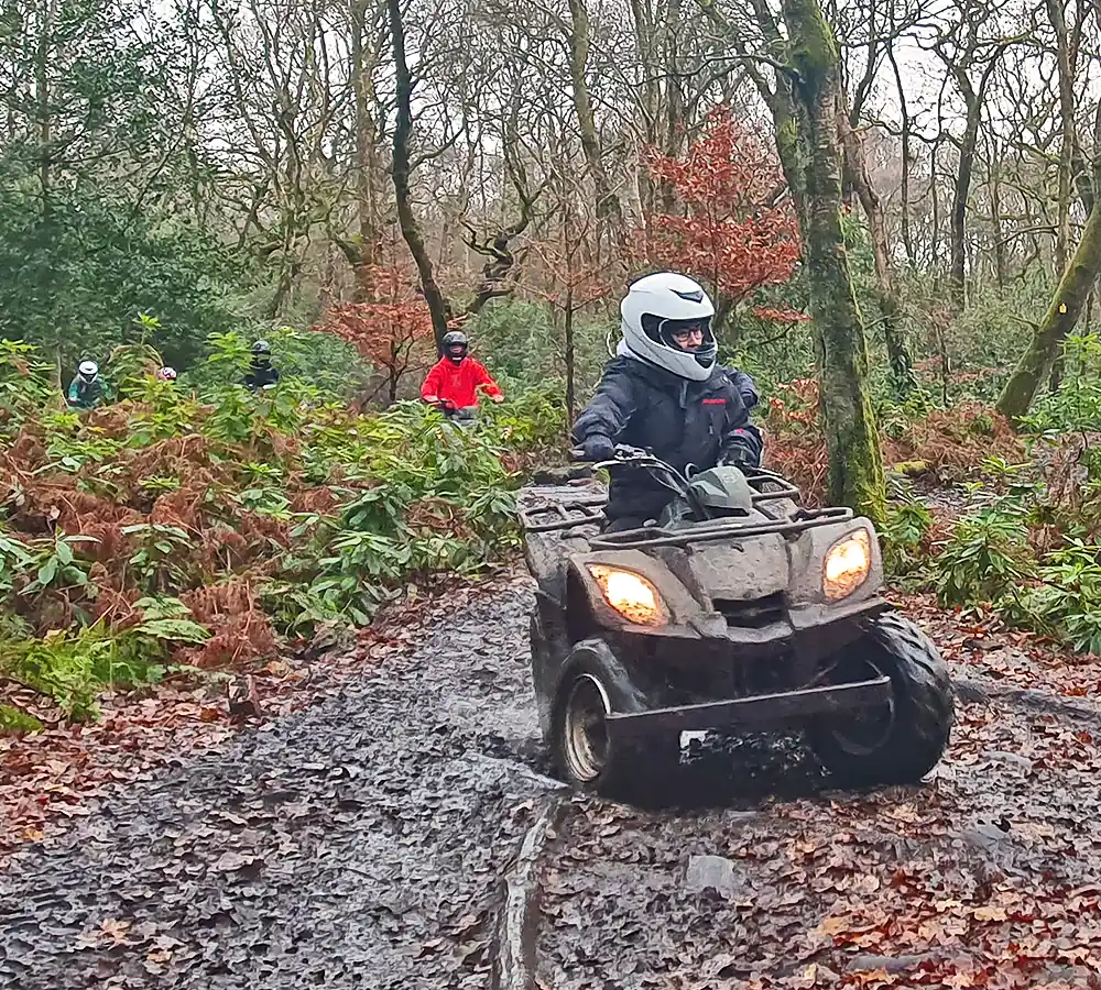 Action shot of a lady driving a quad bike through some mud, with three other riders in the background