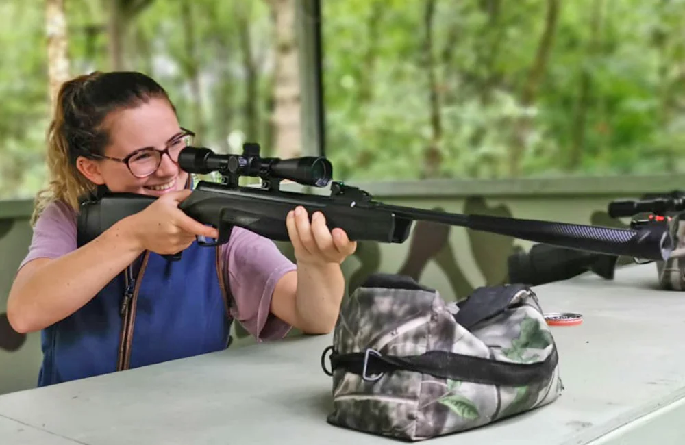 Smiling happy girl shooting an air rifle with a telescopic sight at Adventure Now Manchester