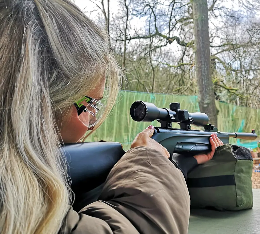 Blonde woman wearing shooting glasses, aiming a Beretta air rifle