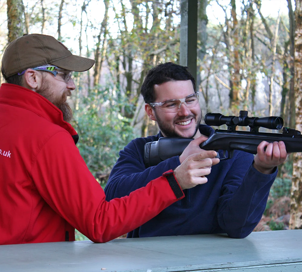 Air Rifle Instructor pointing towards targets on the rifle shooting range. Smiling customer with rifle is looking down the scope