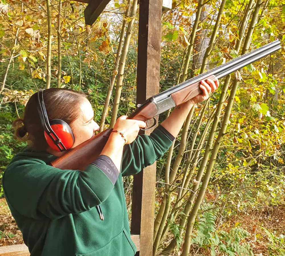 Lady trying clay shooting, pointing shotgun into the sky at target