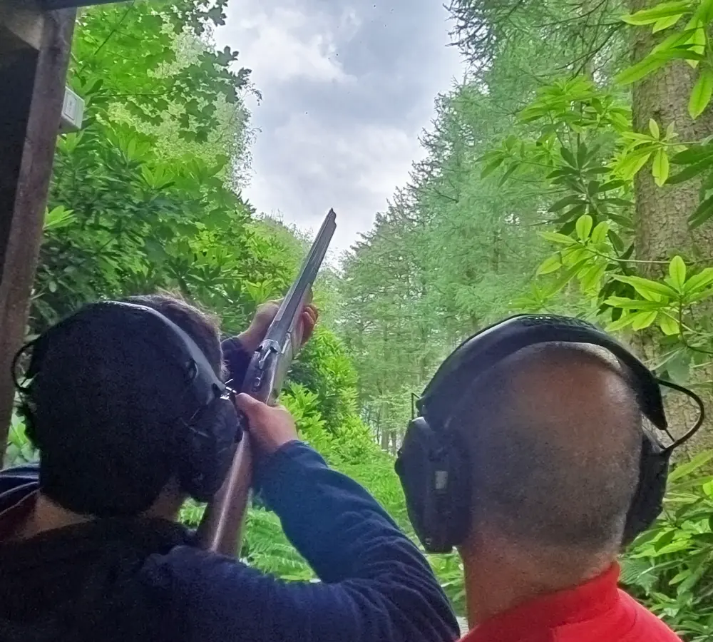 Person aiming shotgun into the sky, with an instructor stood next to them