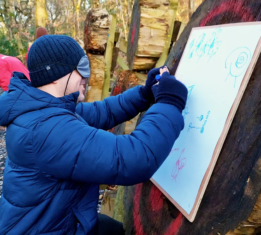 Smiling man wearing a blindfold, drawing on a large canvas as team building activity