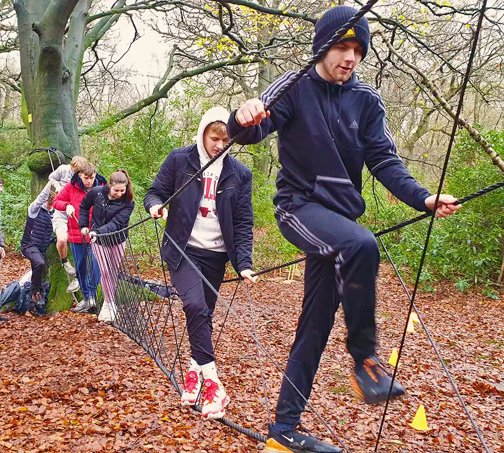 Team activity where people are crossing a rope bridge in a woodland