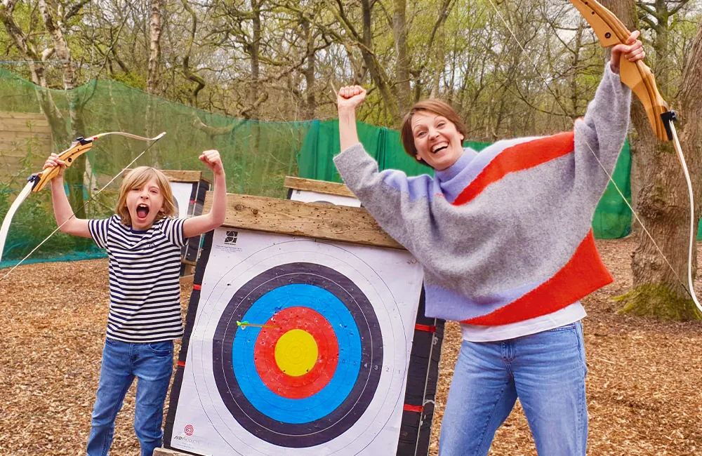 Happy mum and excited child with archery bows and a target at Adventure Now Manchester