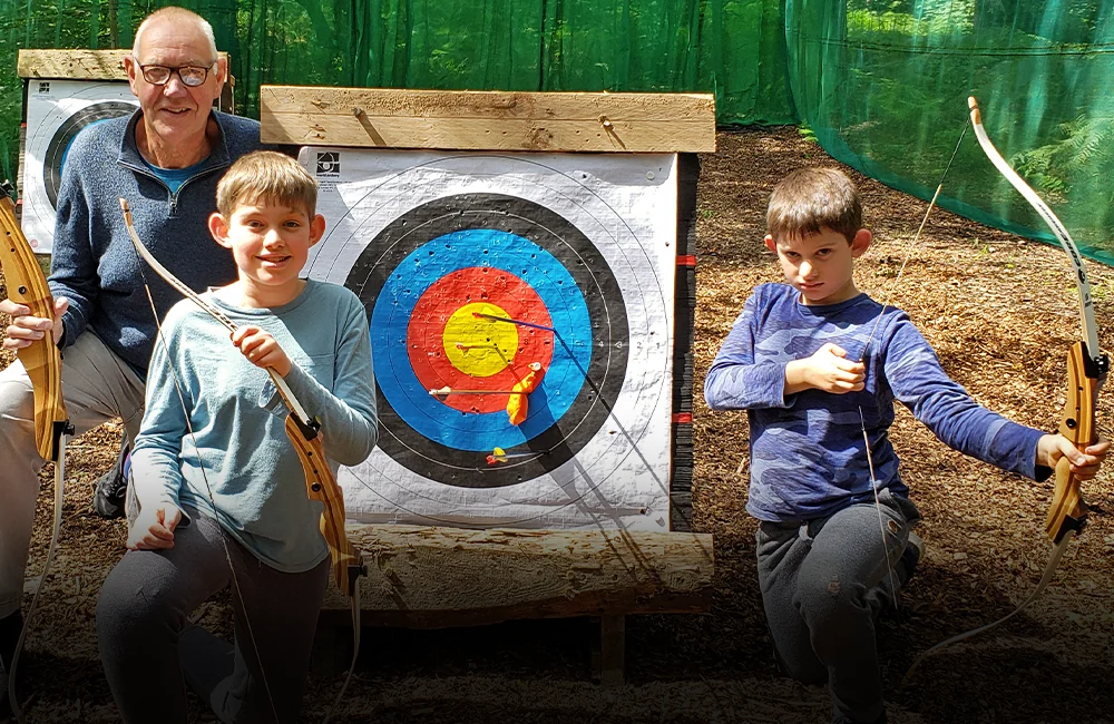 A dad and two kids with bows and an archery target at Adventure Now Manchester