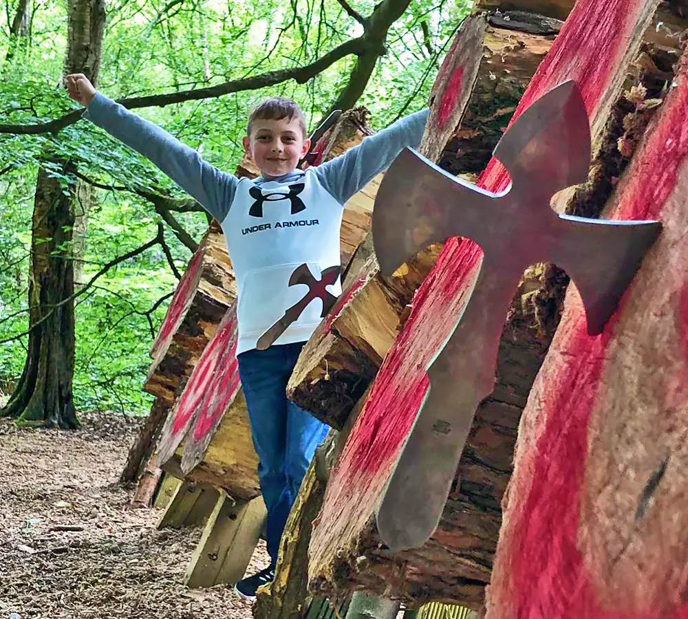 Excited boy with his arms in the air stood with a throwing knife/angel stuck in a wooden outdoor target