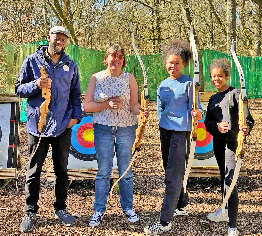 Smiling family with kids holding archery bows, stood in front of outdoor targets