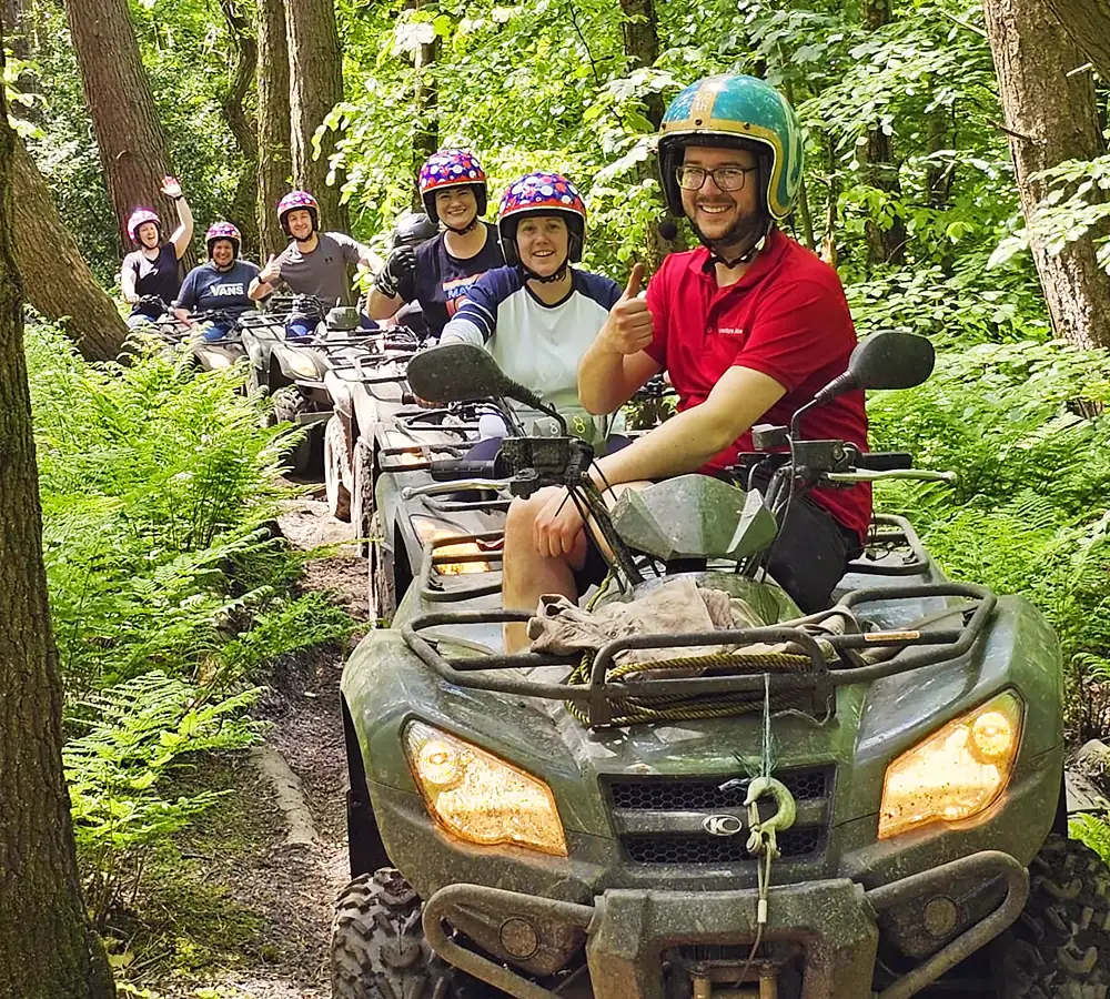 Off-road quad biking group parked in a line smiling at the camera. Instructor at the front is giving a thumbs up.