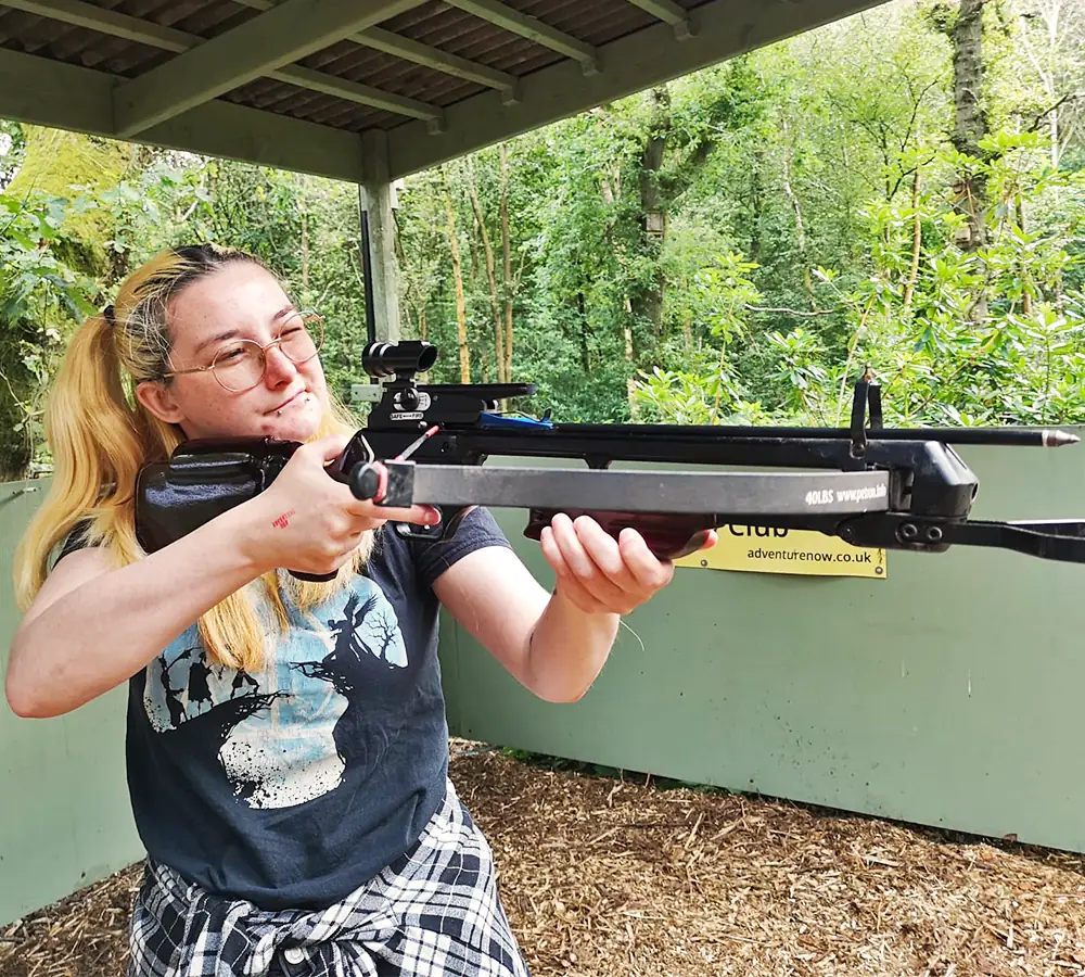 Smiling woman shooting a crossbow on an outdoor shooting range at Adventure Now in Manchester