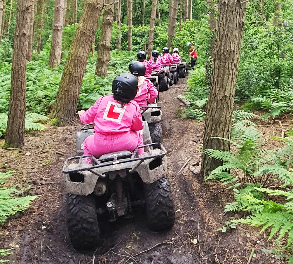 Hen party in a line quad biking. All dressed in pink overalls