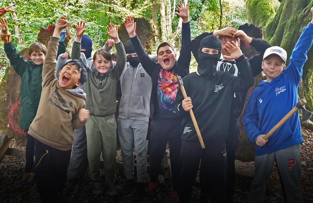 An excited children's party group with their hands up in the air, outside doing axe throwing