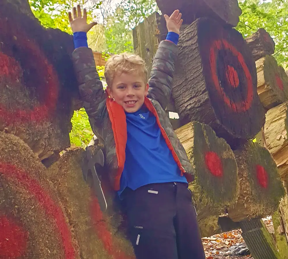 Excited boy with his hands in the air, leaning against a knife target with a throwing angel stuck in it