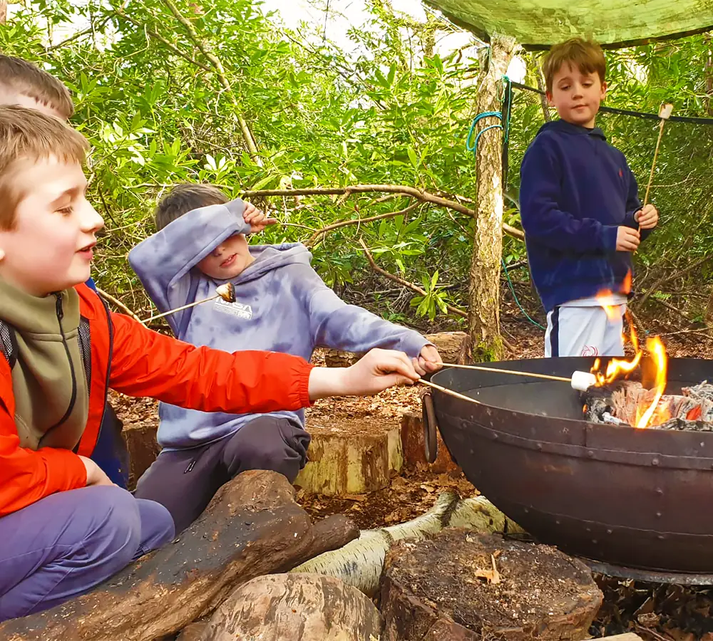 Smiling children roasting marshmallows on a fire in a steel fire pit at Adventure Now in Manchester