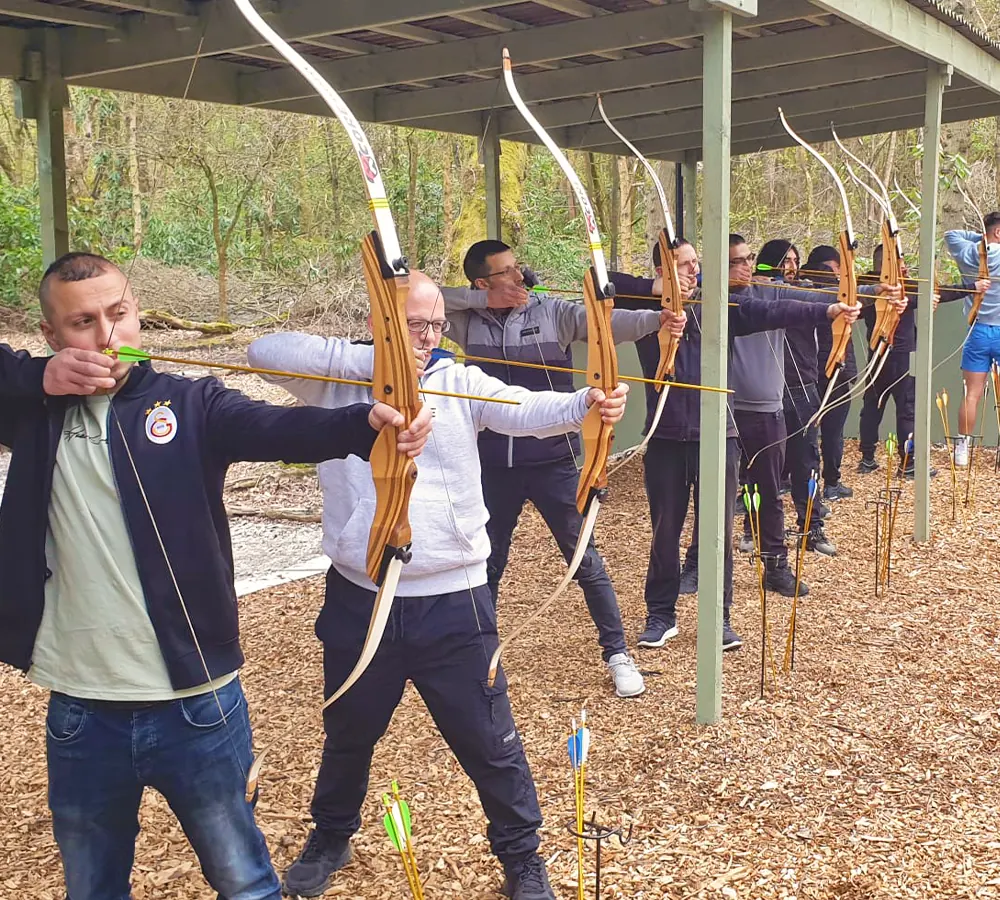 Stag party group doing archery. All aiming bows, stood in outdoor shooting range