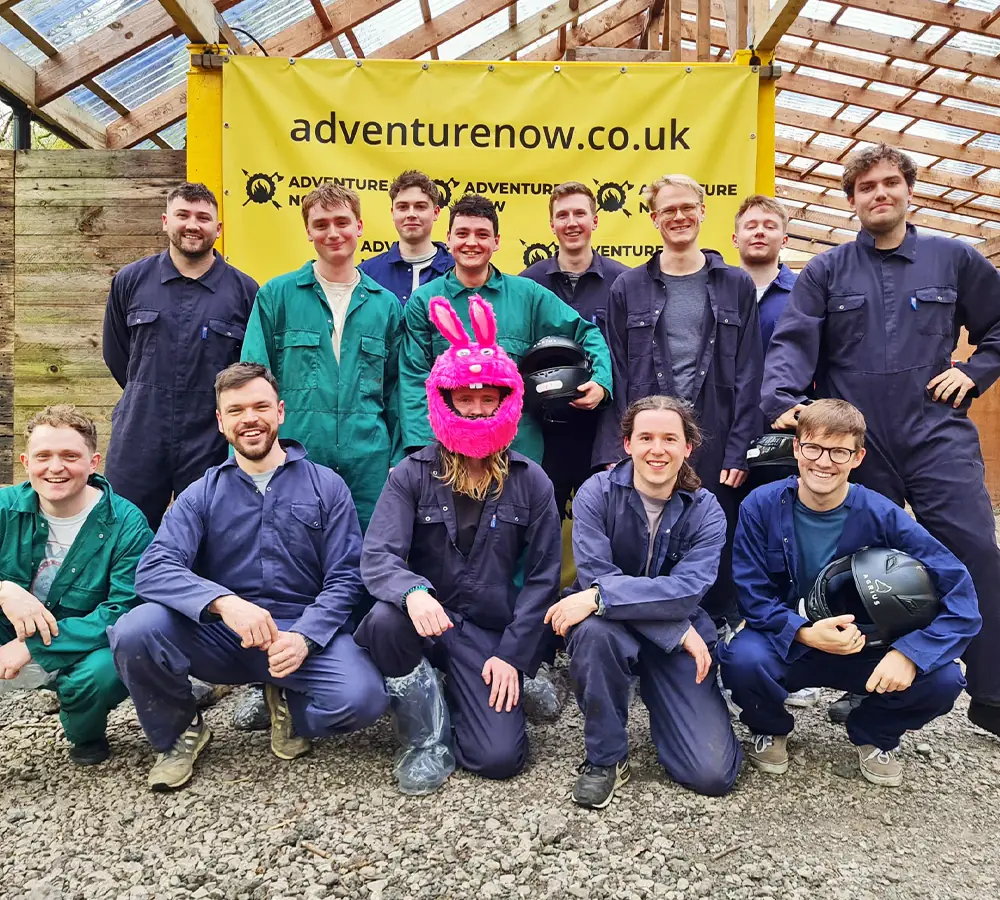 Group of guys on a stag do at Adventure Now posing together after going quad biking. Stag in the middle wearing a pink helmet cover