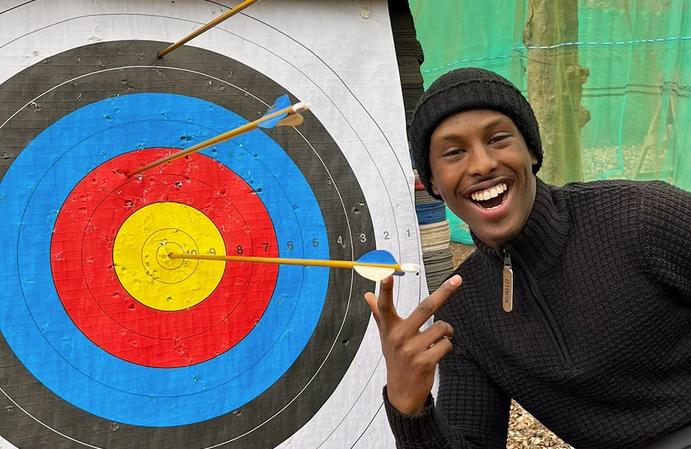 Smiling man next to an archery target with arrows shot into it, one arrow in the bullseye