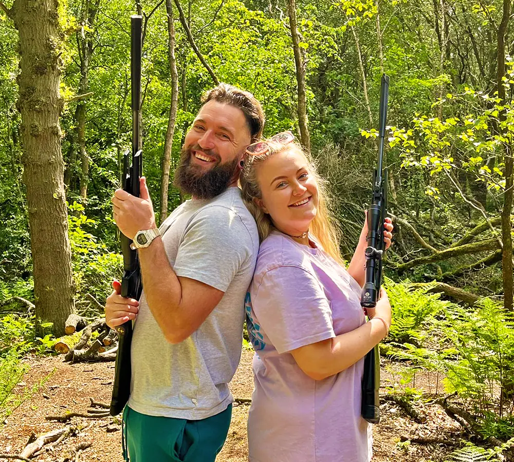 Happy couple stood back to back holding air rifles after shooting the for an hour