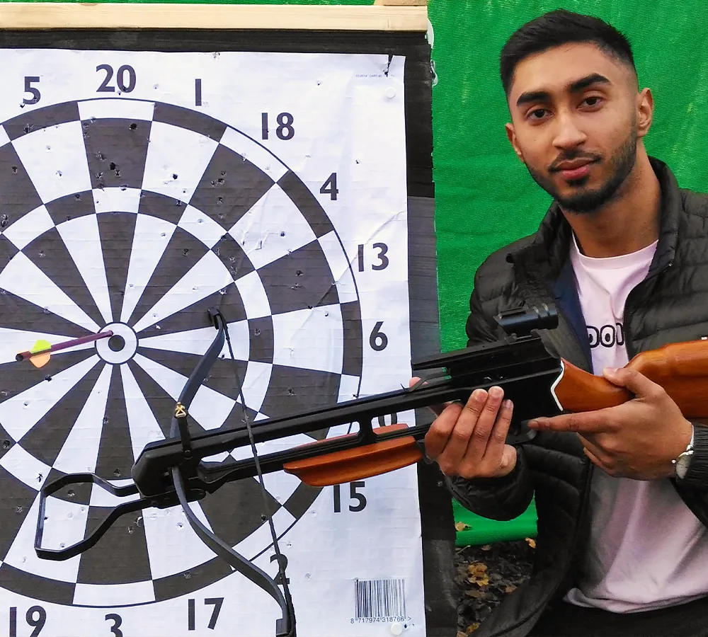 Man posing with wooden crossbow and crossbow target at Adventure Now in Manchester