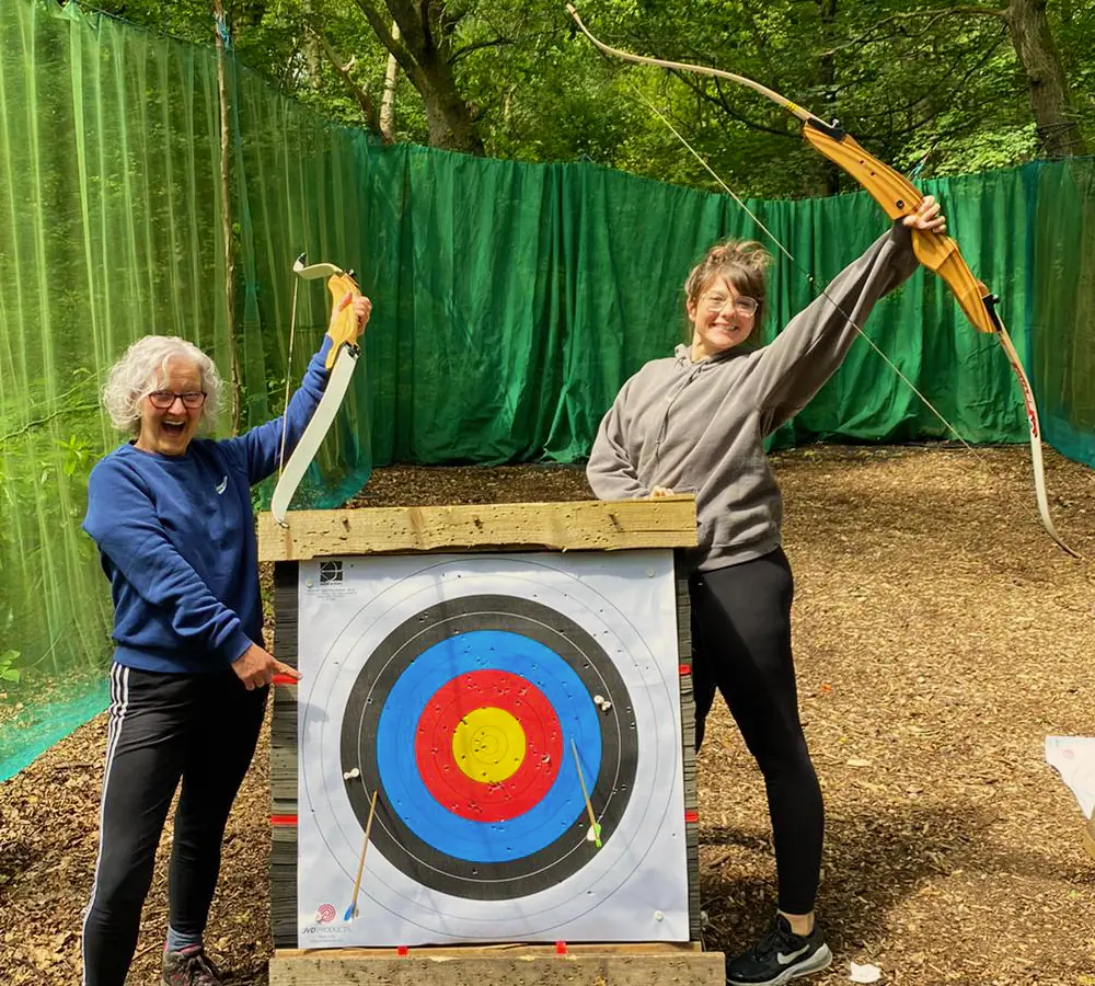 Excited mum and daughter with archery bows and target, pointing at arrows