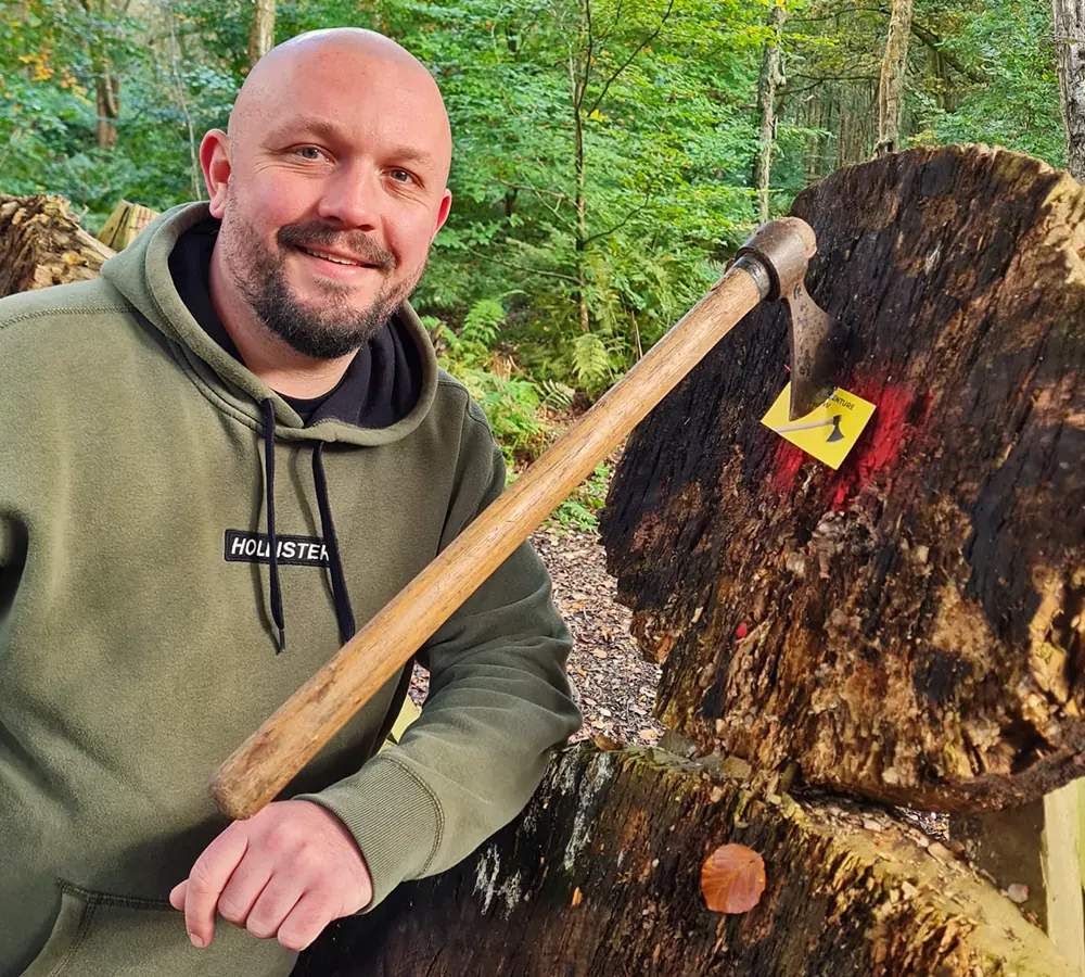 Smiling man leaning on an axe throwing target, throwing axe is stuck in the target