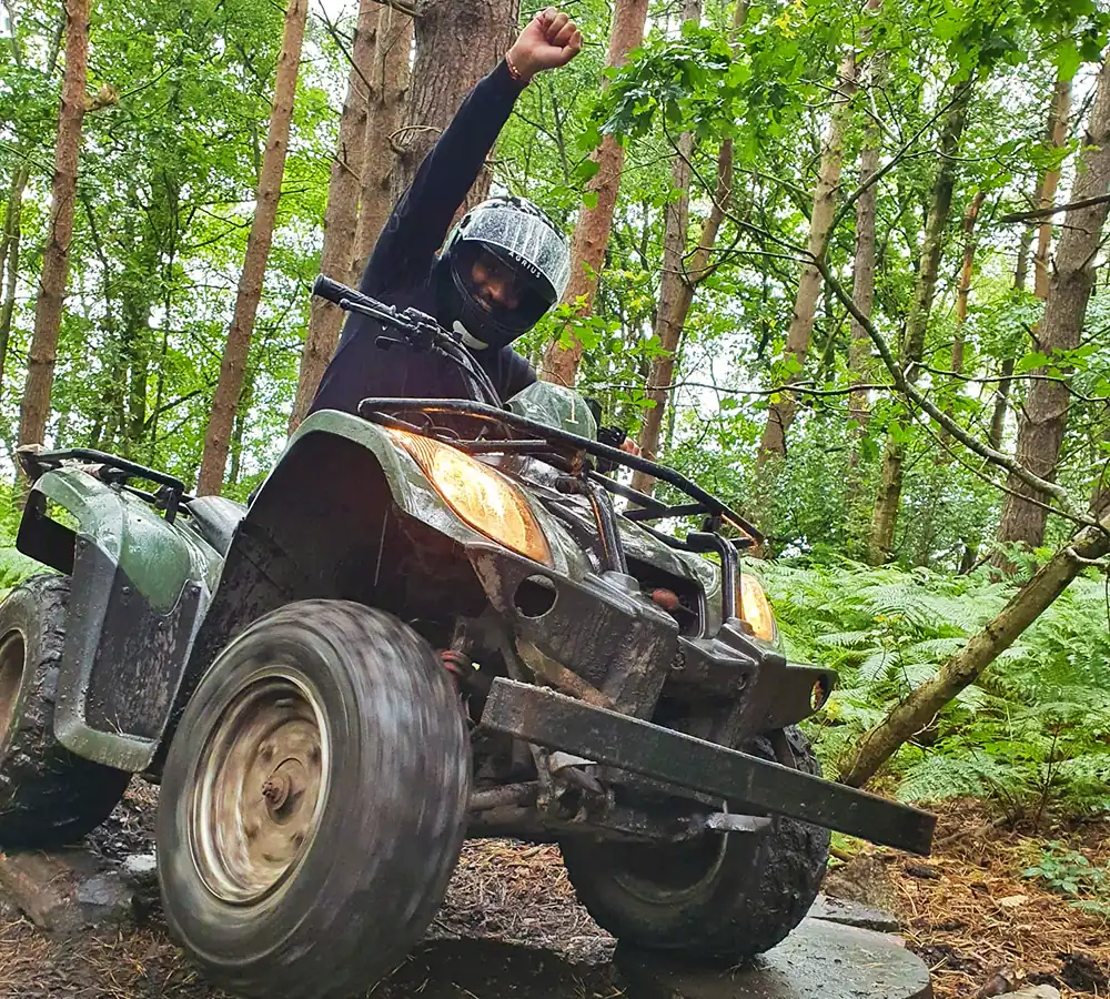 Man on a quad bike with his fist in the air out of excitement. In a woodland setting